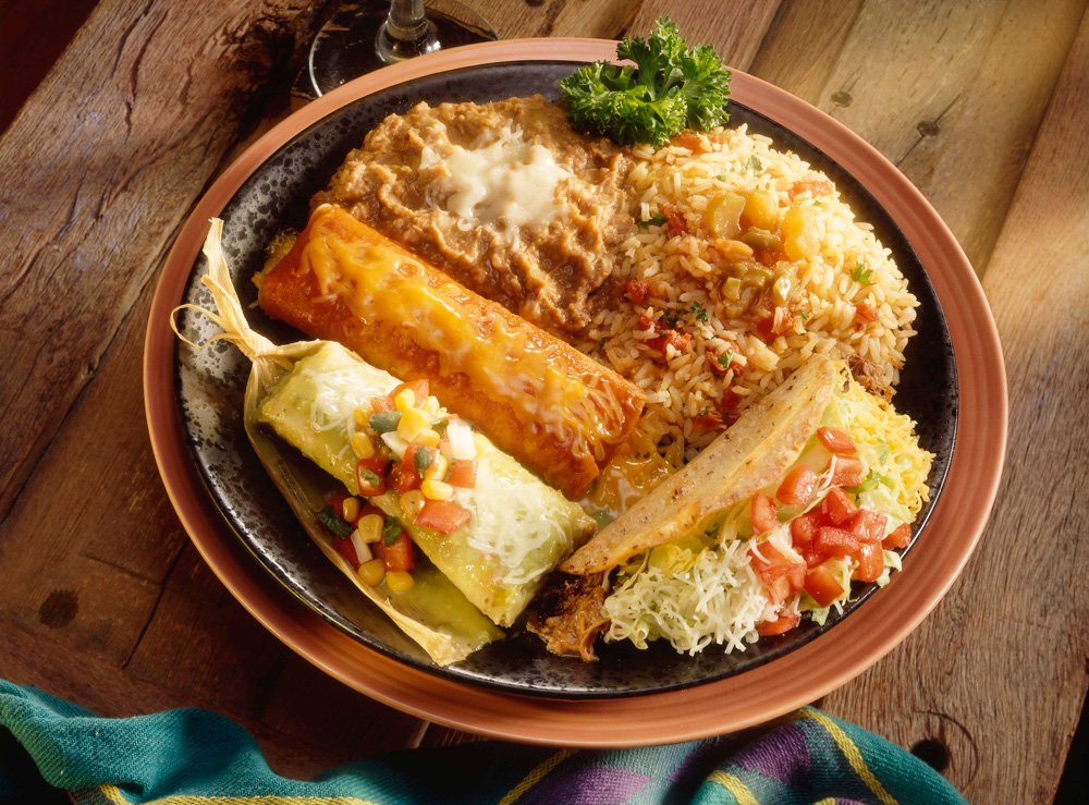 Plate of Mexican food with enchiladas, rice, refried beans, and garnishes