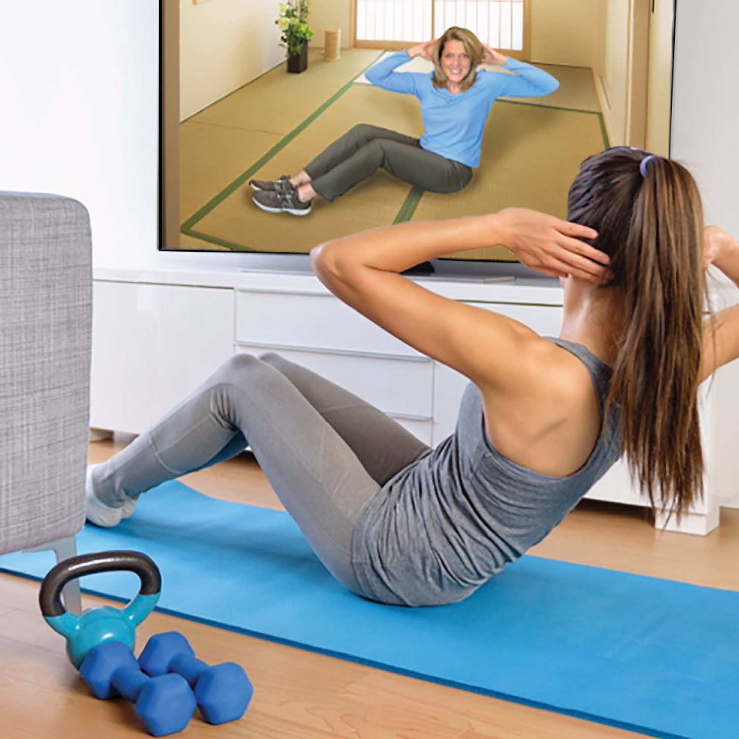 Woman doing sit-ups on a mat while following a workout video on TV