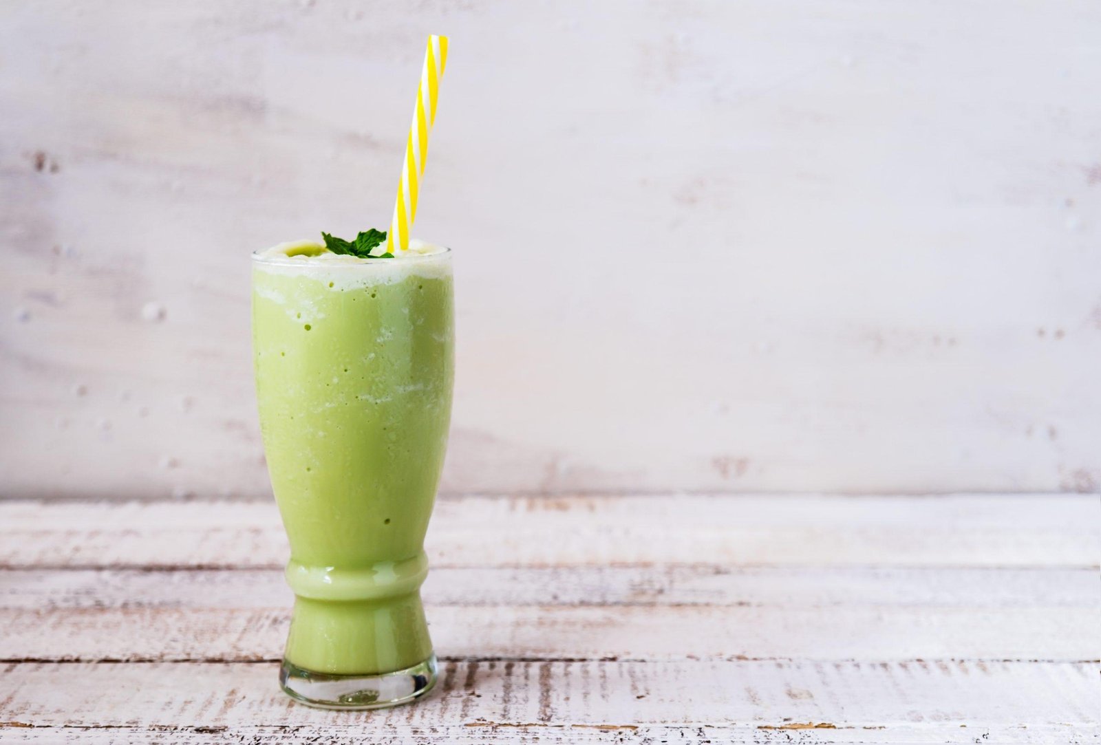 Green smoothie in a tall glass with a yellow-striped straw and mint garnish