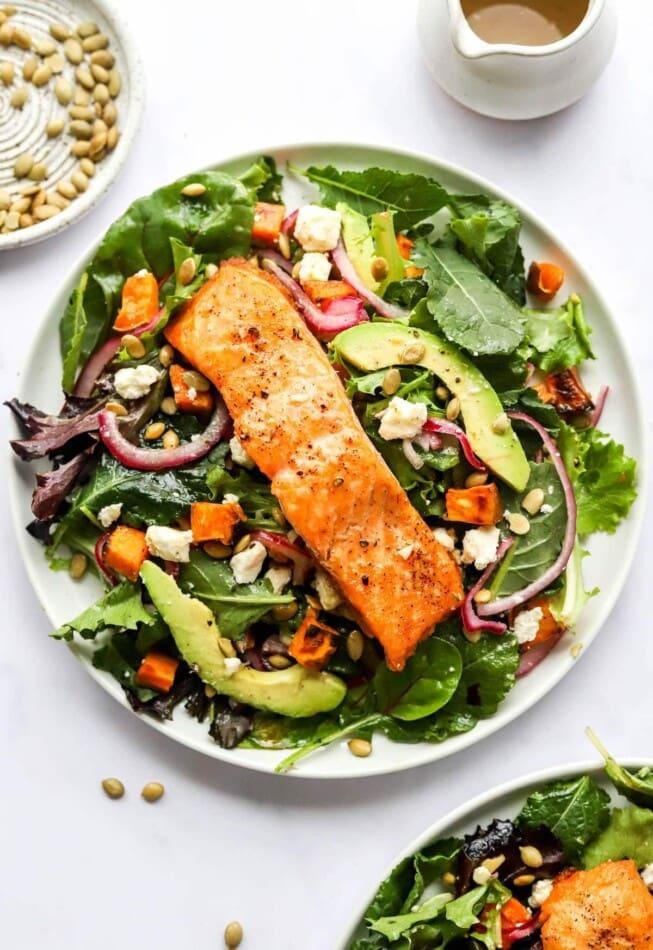 Salmon fillet on a mixed green salad with avocado, roasted vegetables, red onion, and seeds