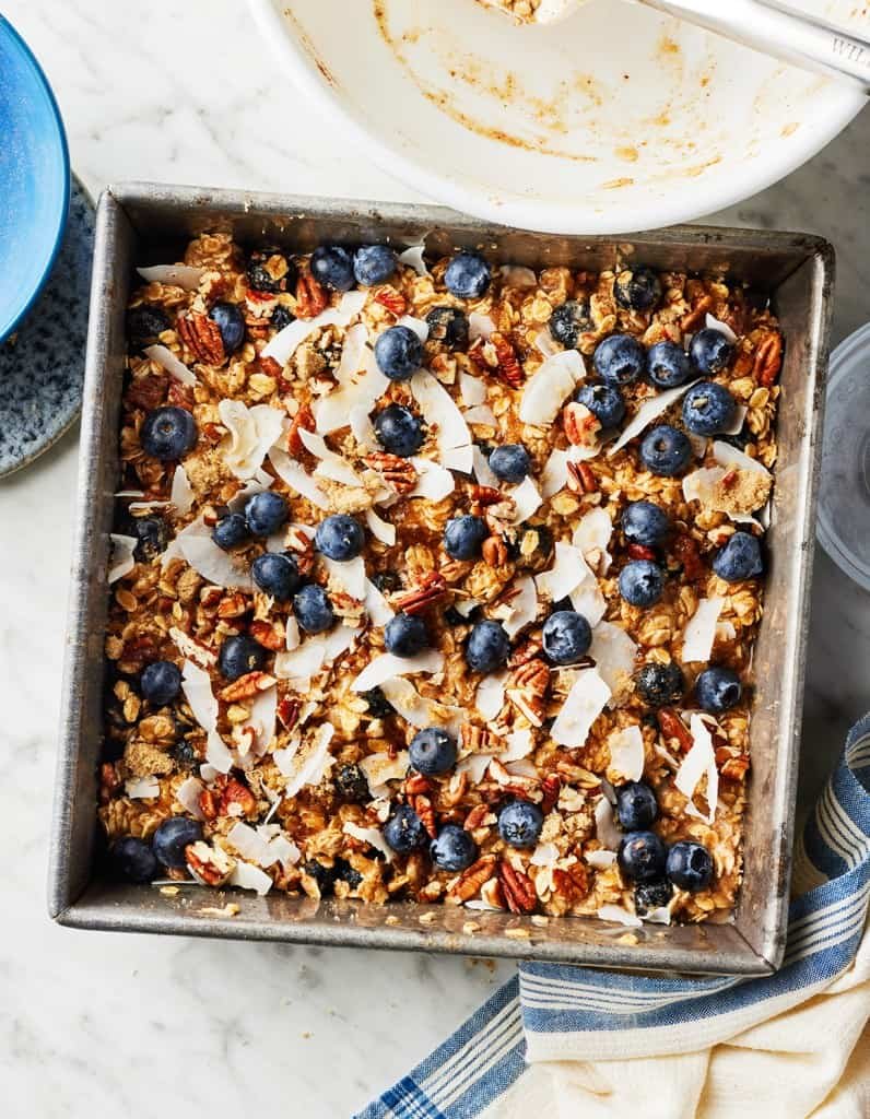 Baked oatmeal topped with blueberries, pecans, and coconut flakes in a square pan