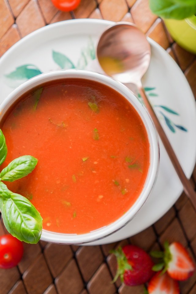 Bowl of tomato soup garnished with basil, served on a plate with a spoon
