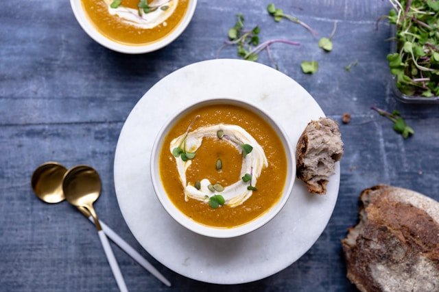 Butternut soup topped with cream and microgreens, served with bread on a plate