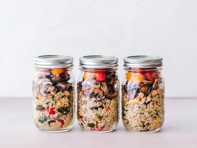 Three mason jars filled with layered quinoa, vegetables, and mushrooms