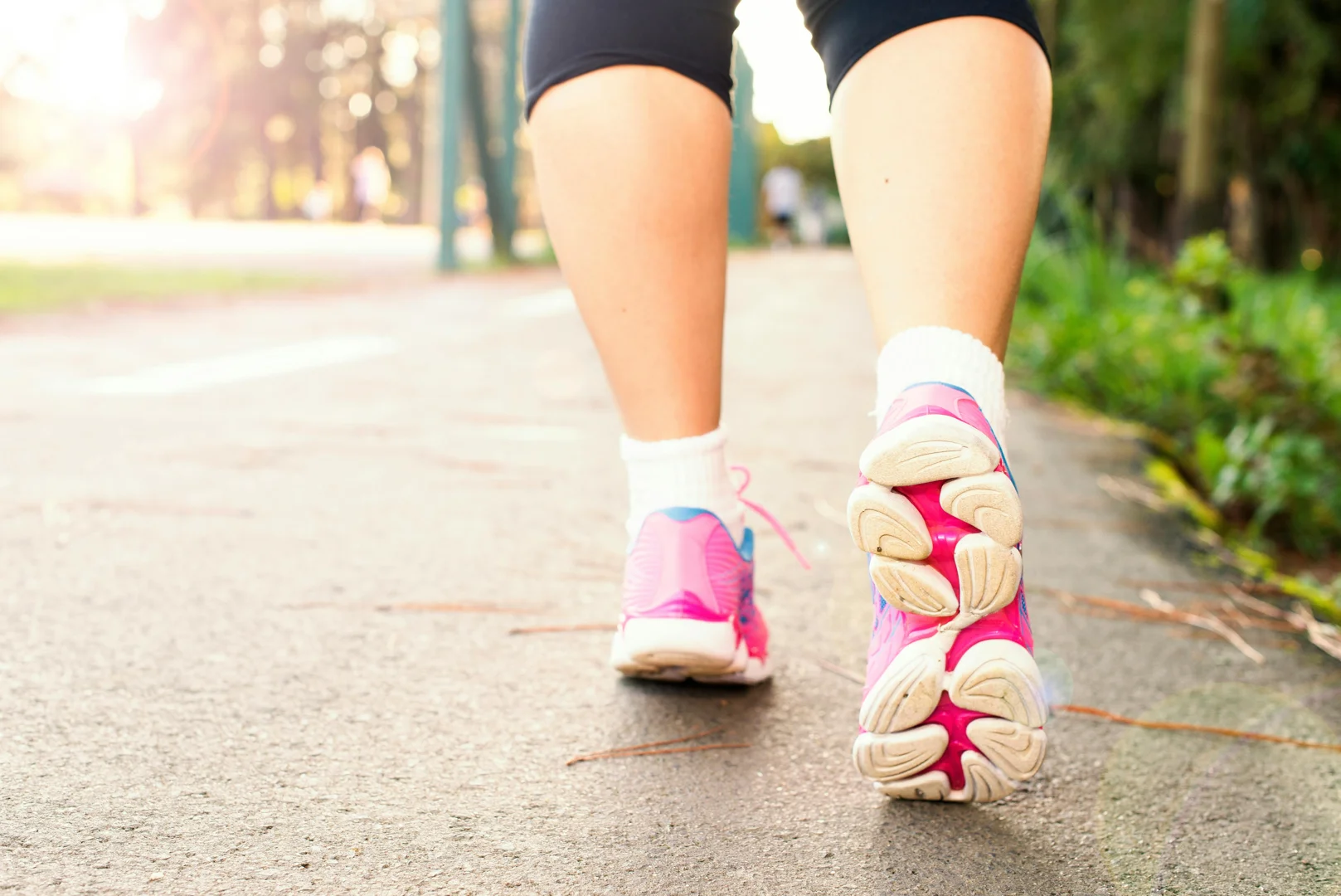 Person walking on a sunlit path in pink running shoes